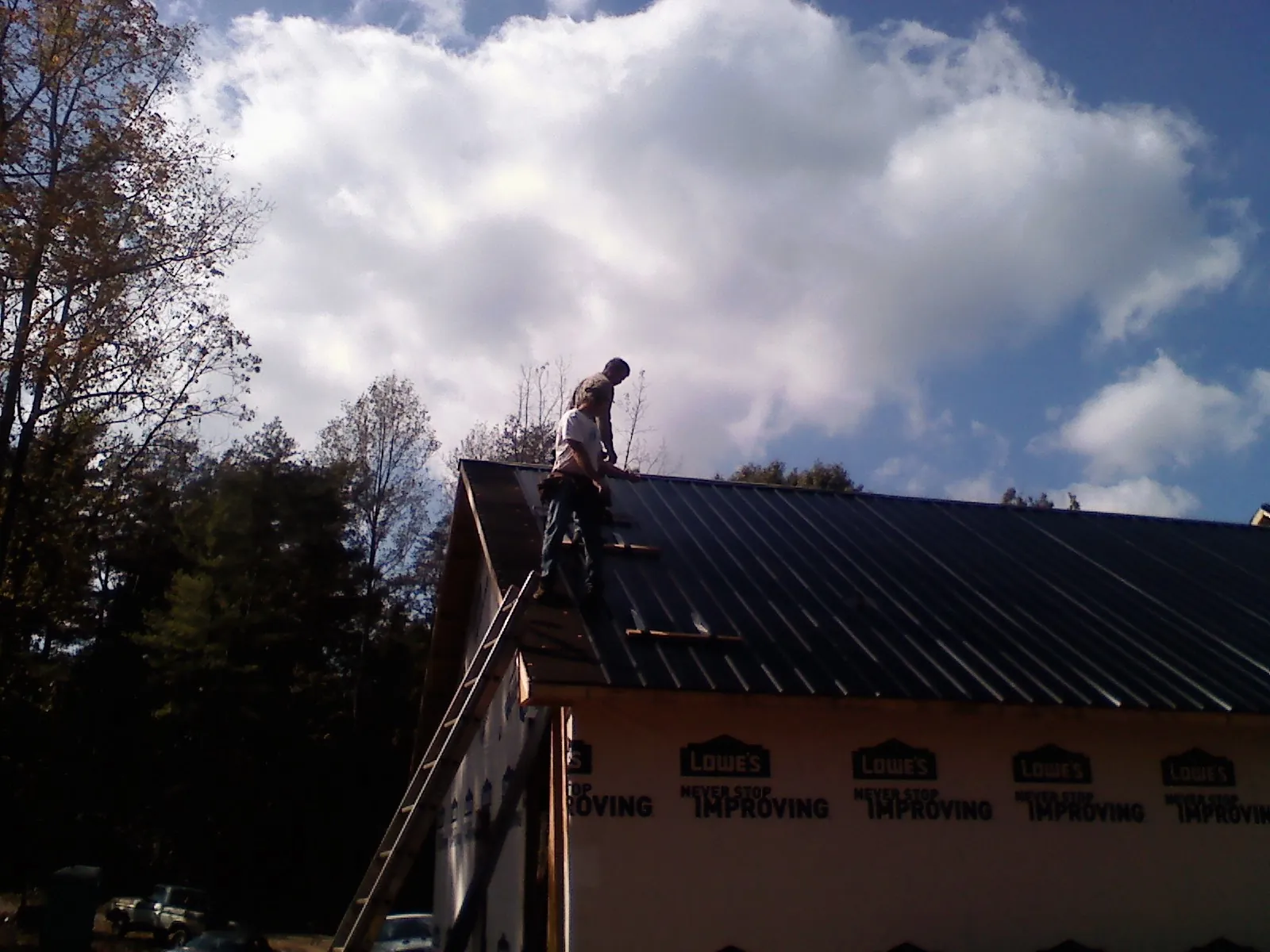 Roofer fastening dark metal panels high against a cloudy sky, from a Roof Inspection job in Yonkers