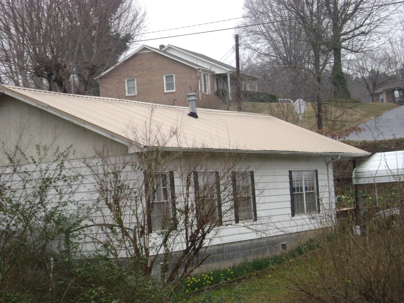 Tan metal roof on a white sided house set into a hillside — Commercial Roofing by Roofing Brothers in Yonkers